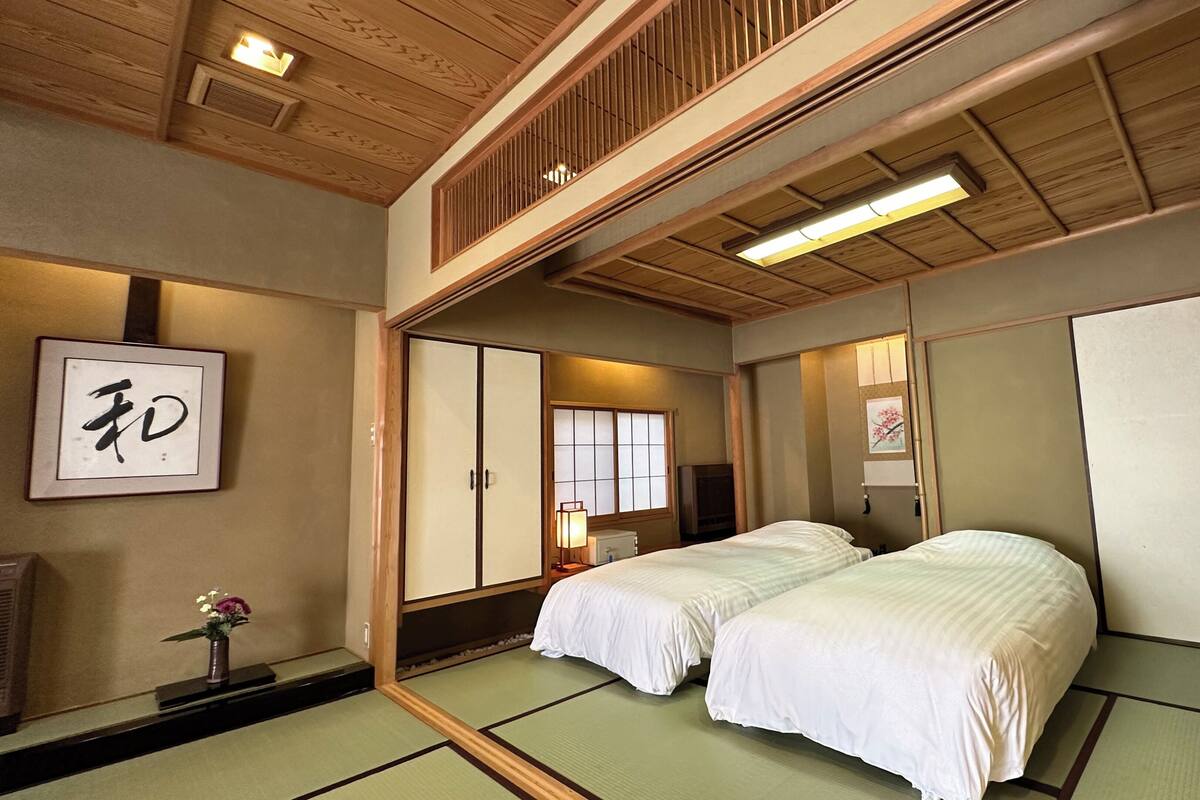 Una habitación japonesa tradicional con suelo de tatami, un futón, puertas correderas y un televisor.