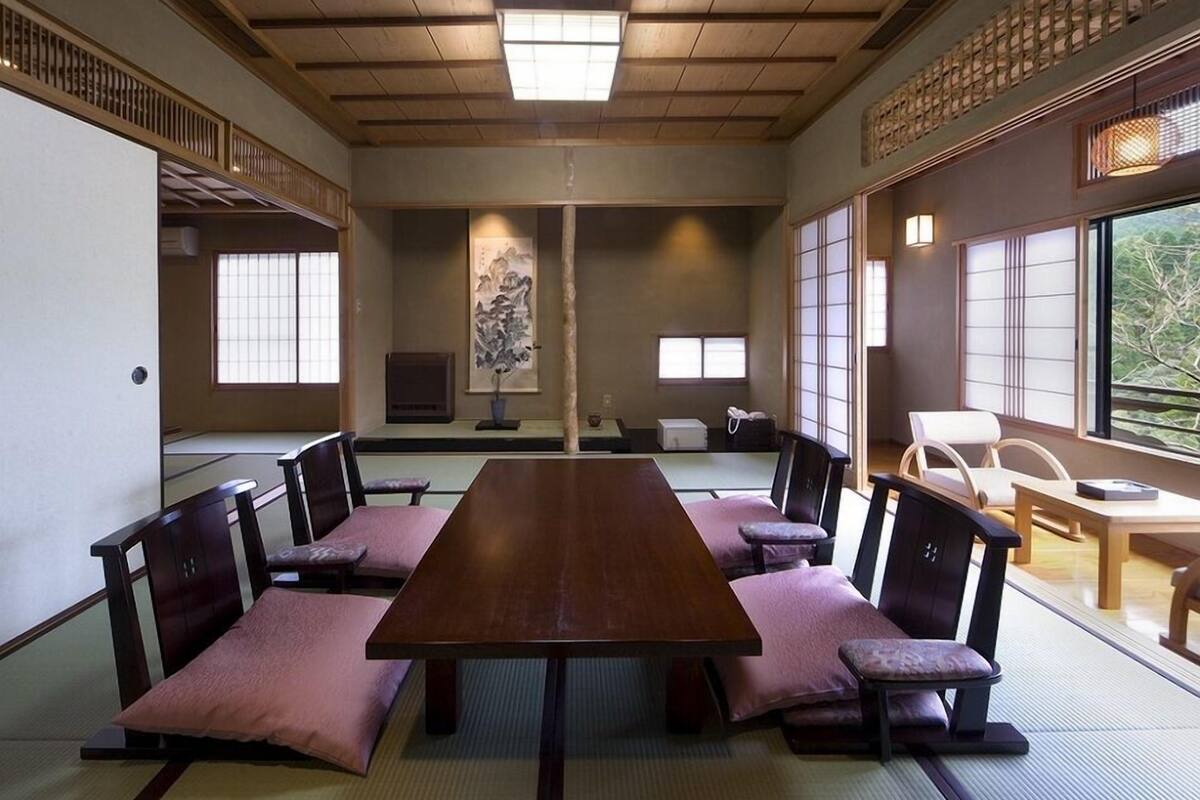Una habitación japonesa tradicional con suelo de tatami, una mesa de madera larga y sillas de madera bajas.