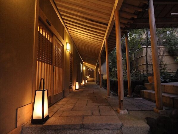 A corridor with wooden pillars and lanterns, leading to a traditional building.