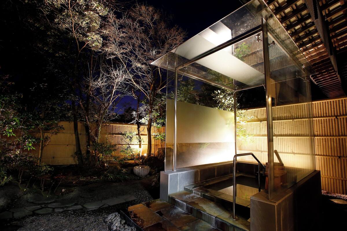 Un baño moderno al aire libre con recinto de vidrio, cerca de madera y sendero de piedra.