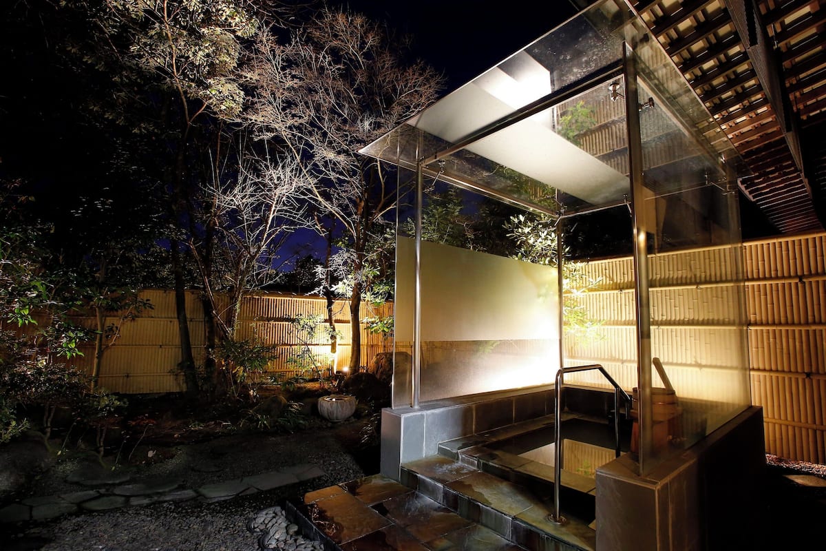 A modern outdoor bathroom with a glass enclosure, a wooden fence, and a stone pathway.