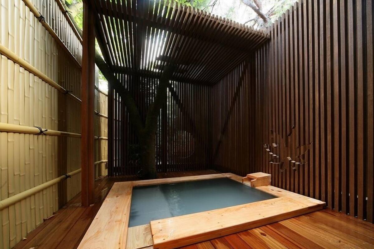 Un área de baño termal con suelo de madera, un banco de madera y una valla de bambú.