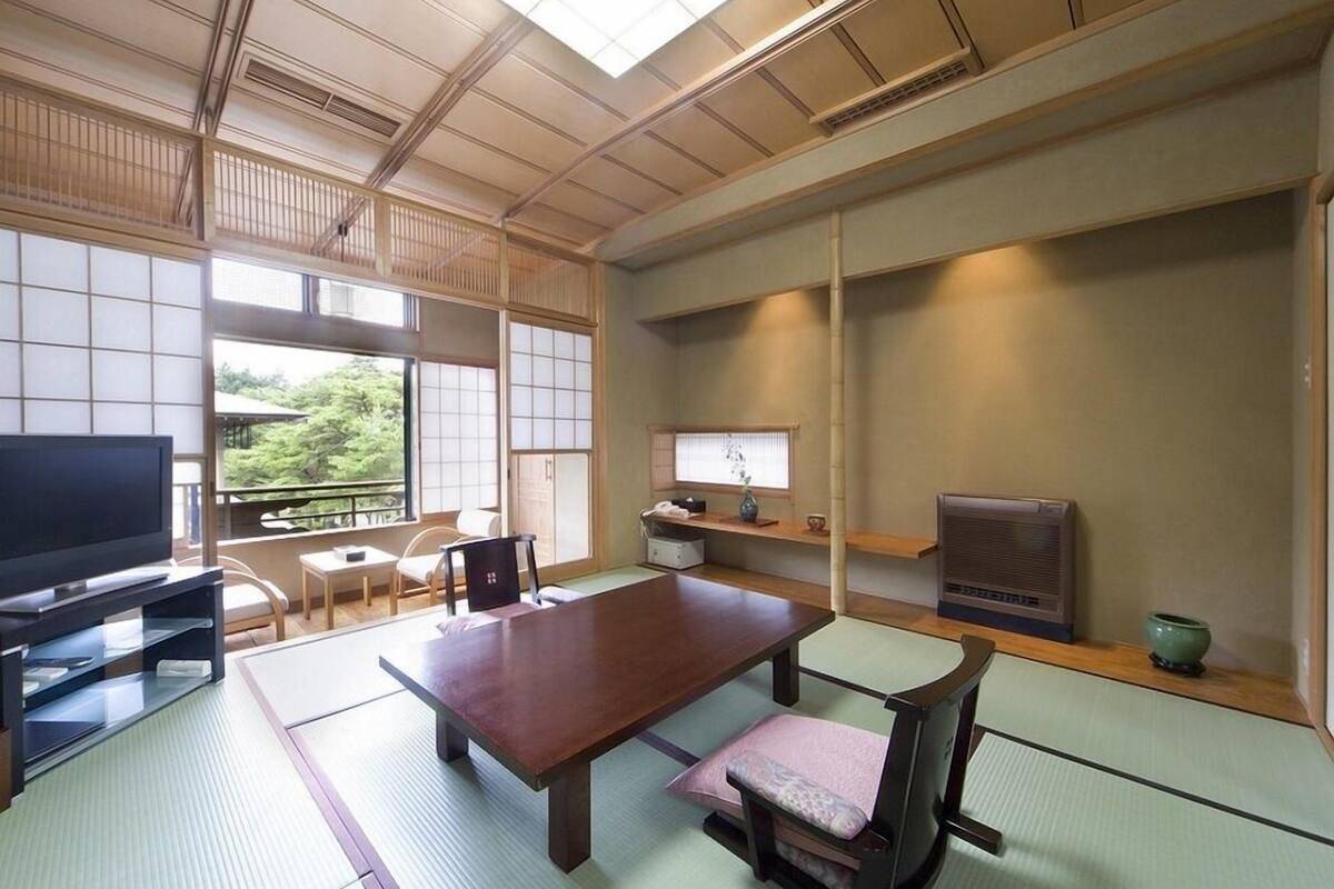 Una habitación japonesa tradicional con suelo de tatami, una mesa baja, un televisor y una puerta corredera.