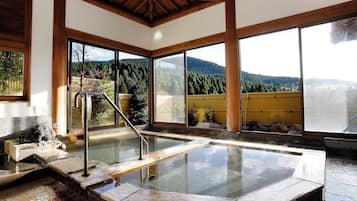 A hot spring area with wooden beams, a stone platform, and a view of a forested mountain.