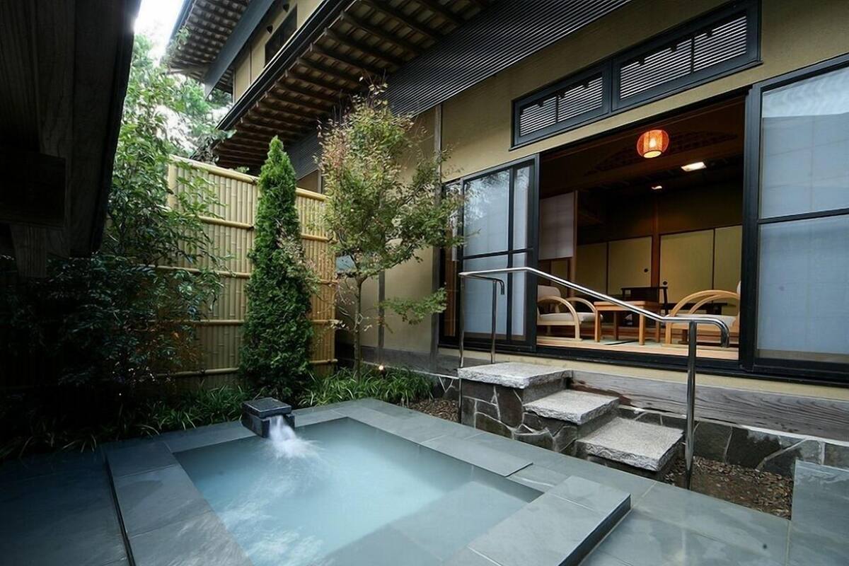 Un espacio exterior moderno con un manantial termal, escalones de piedra y una edificación tradicional japonesa.