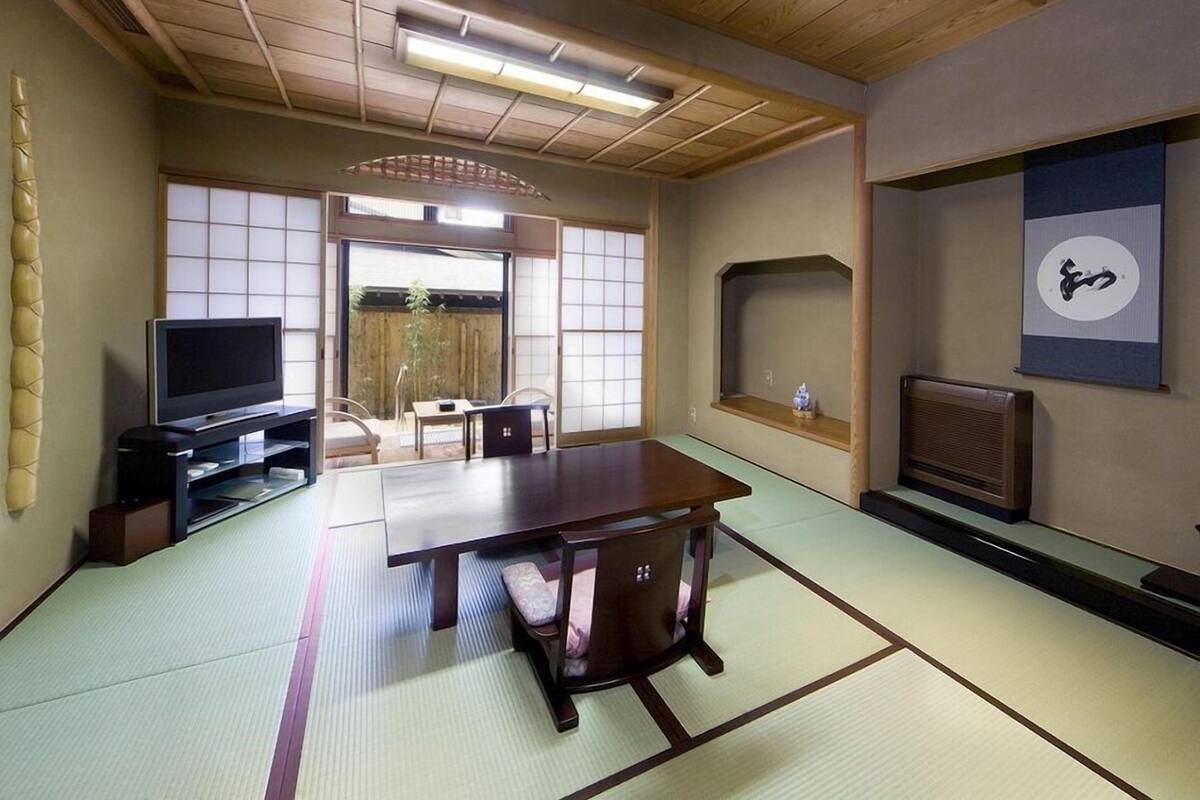 Una habitación tradicional japonesa con tatamis, un televisor, asientos en tatami, una puerta corredera y una pantalla shoji.