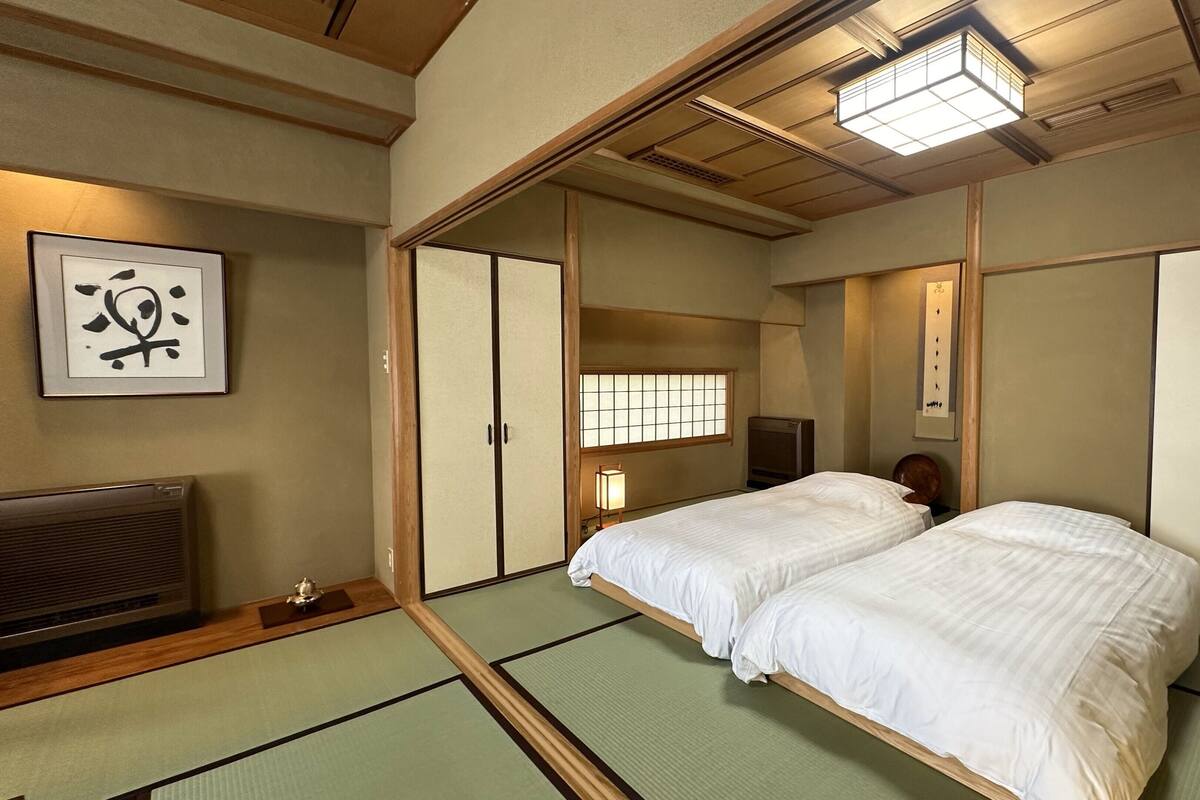 Una habitación tradicional japonesa con suelo de tatami, futón, puertas correderas y ventilador de techo.