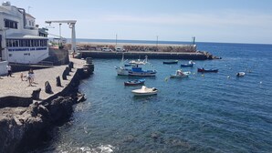 Cena costeira com um restaurante chamado 'RESTAURANTE LOS ABRIGOS' à esquerda, barcos atracados na água e uma vista clara do mar.