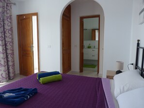 Une chambre à coucher avec un lit, une table de chevet, une lampe et une salle de bain visible à travers une arche.