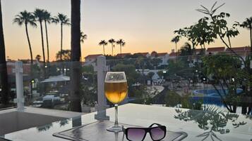 Uma varanda com uma mesa de vidro, uma cerveja e um par de óculos de sol.