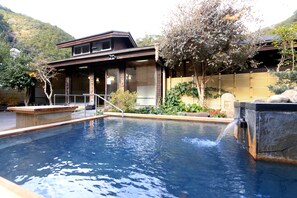 Piscina com cascata, cercada por um muro de madeira e um edifício com grandes janelas.