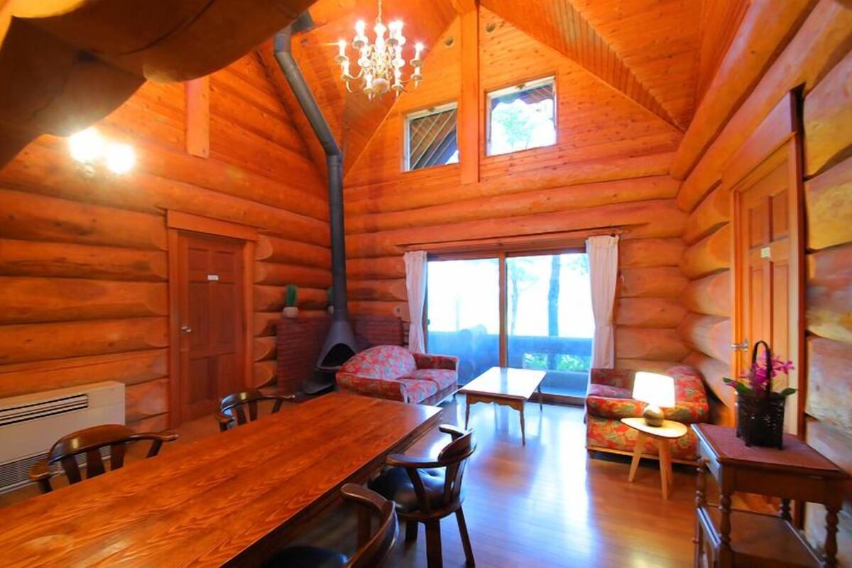 A log cabin interior with a dining area, a fireplace, and a large window.