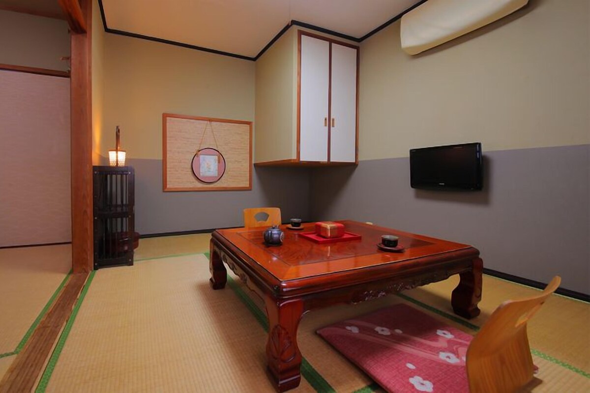A traditional Japanese room with tatami flooring, a low wooden table, a television, and a cabinet.