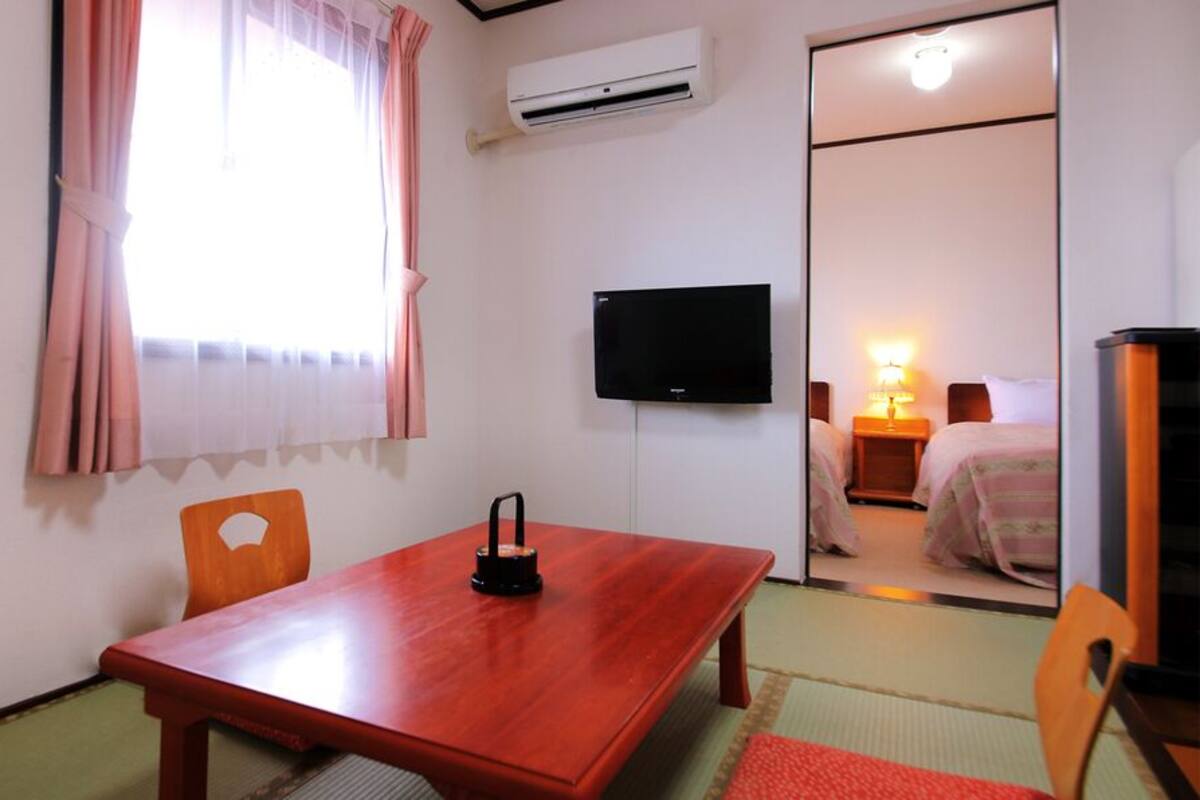 A hotel room with a wooden table, a TV, a bed, and a sliding door leading to another room.