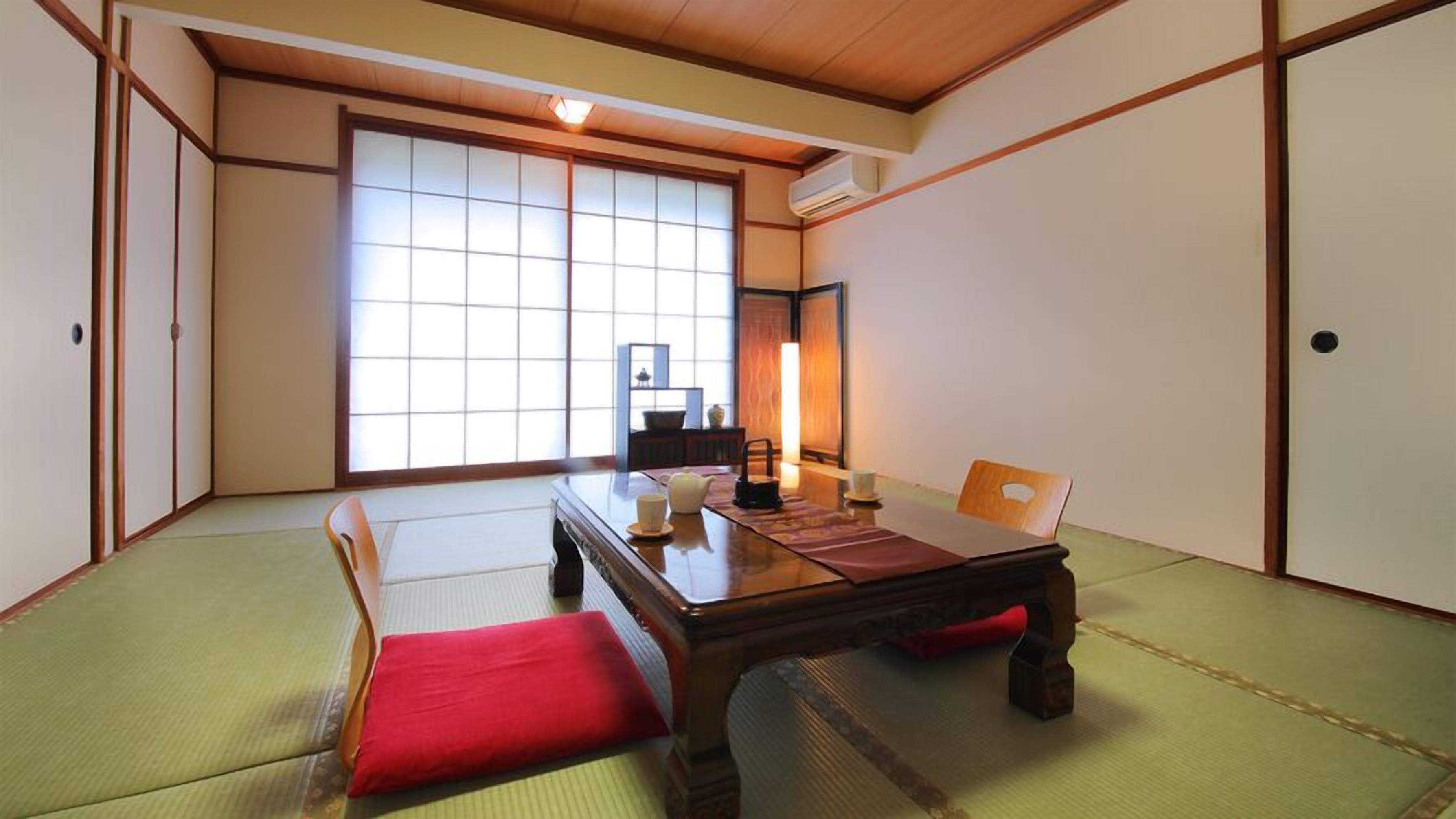 A tatami mat room with a low table, cushions, and sliding doors.