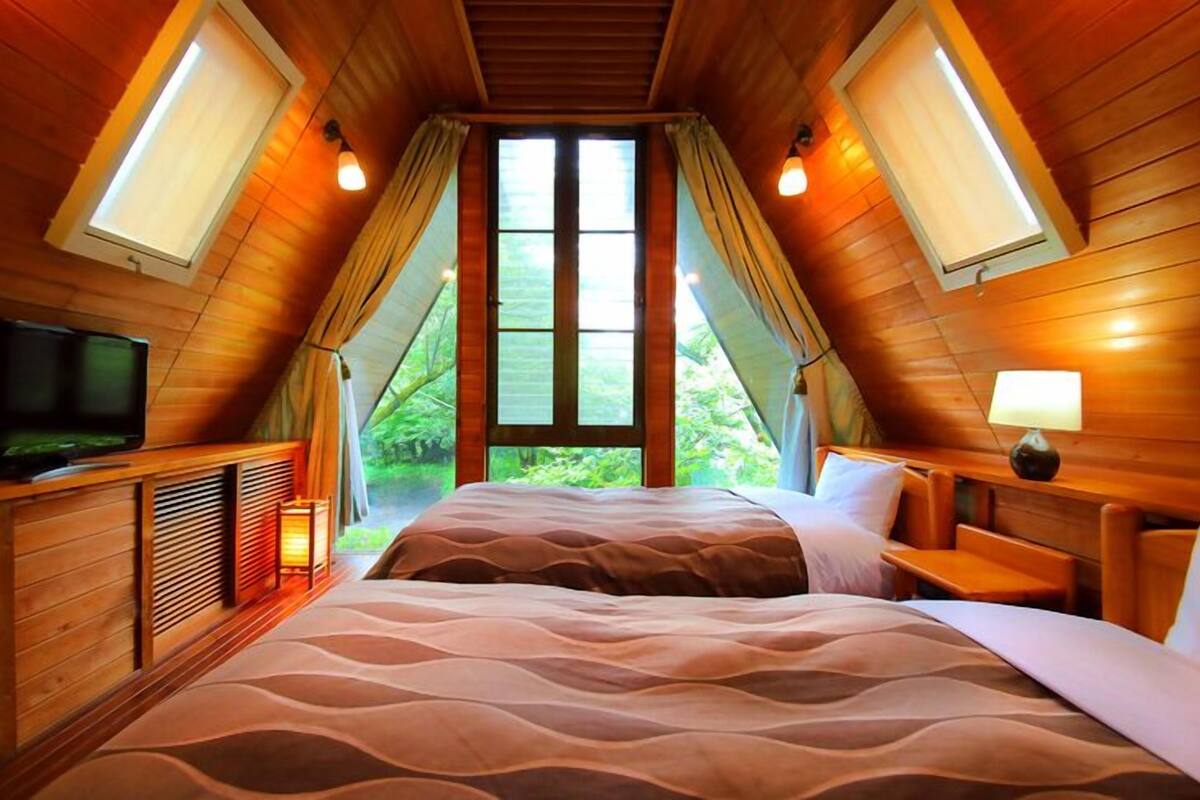 A cozy bedroom with a bed, a TV, and a window with curtains.