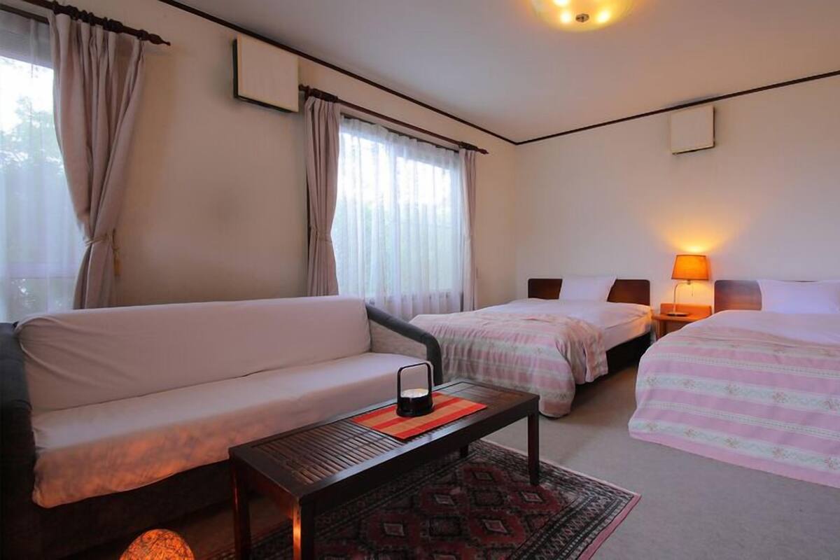 A hotel room with a sofa, two single beds, a small table, and a lamp.