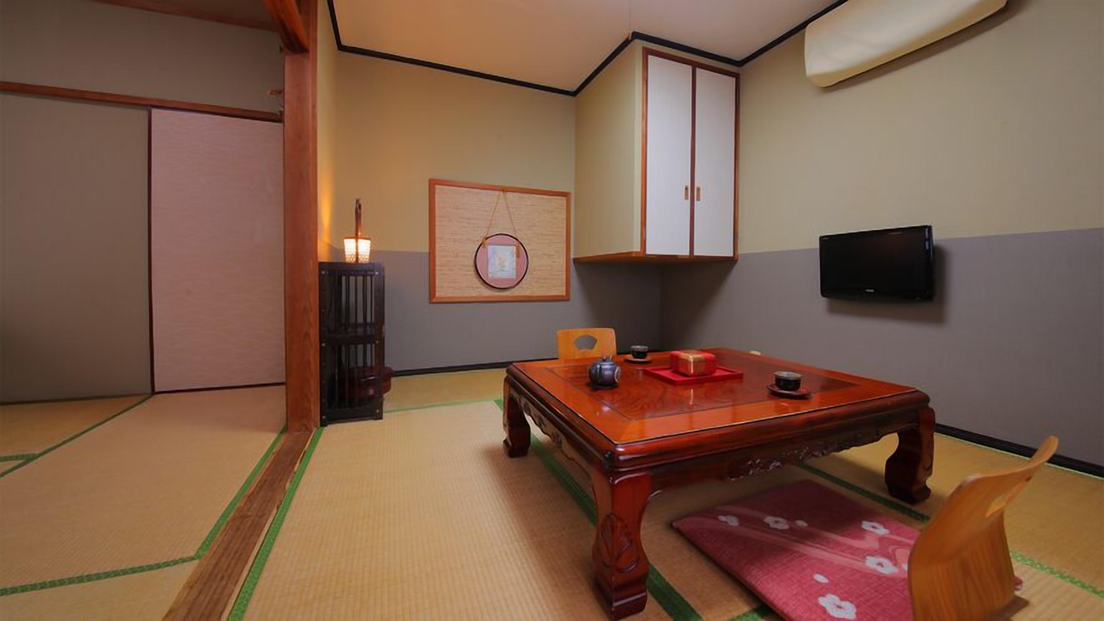 A traditional Japanese room with tatami flooring, a low wooden table, a television, and a cabinet.