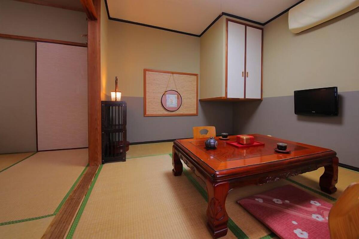 A traditional Japanese room with tatami flooring, a low wooden table, a television, and a cabinet.
