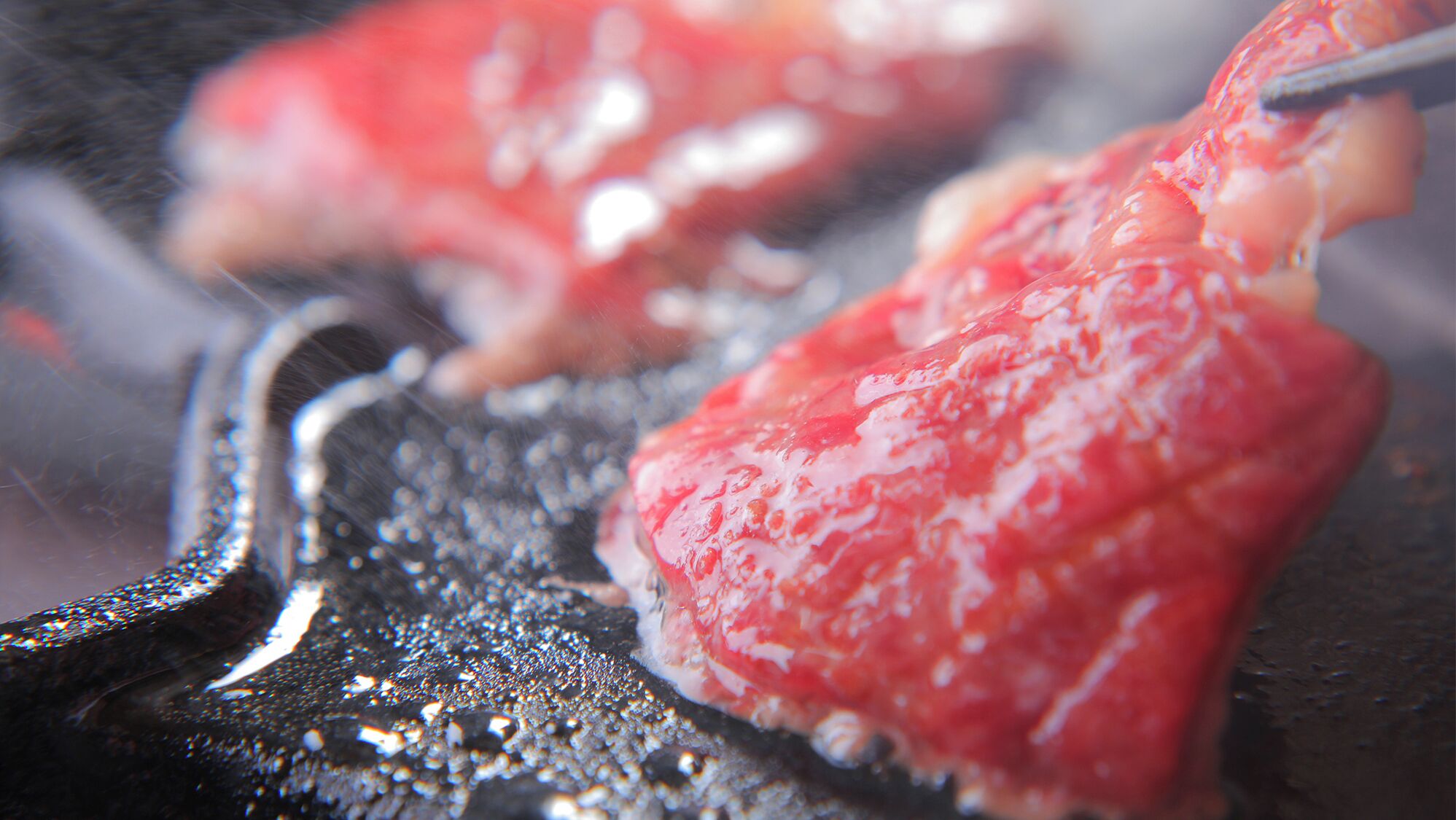 Gros plan sur une étape de la préparation d’un plat, mettant l’accent sur une substance rouge et brillante qui cuit dans une poêle.