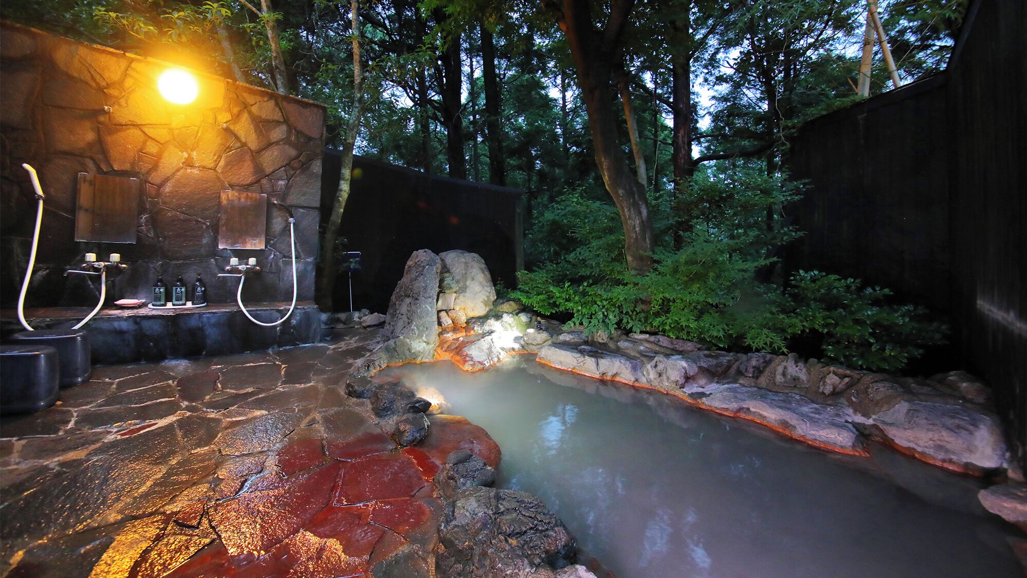 Een bronnenlandschap van steen met een stenen muur, een houten bank en een kleine waterval.