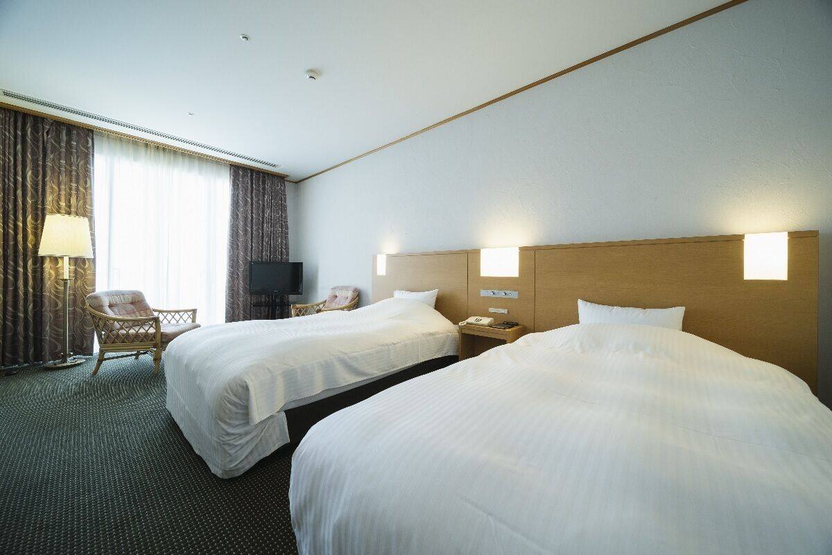 A hotel room with two beds, a chair, a desk, and a television.