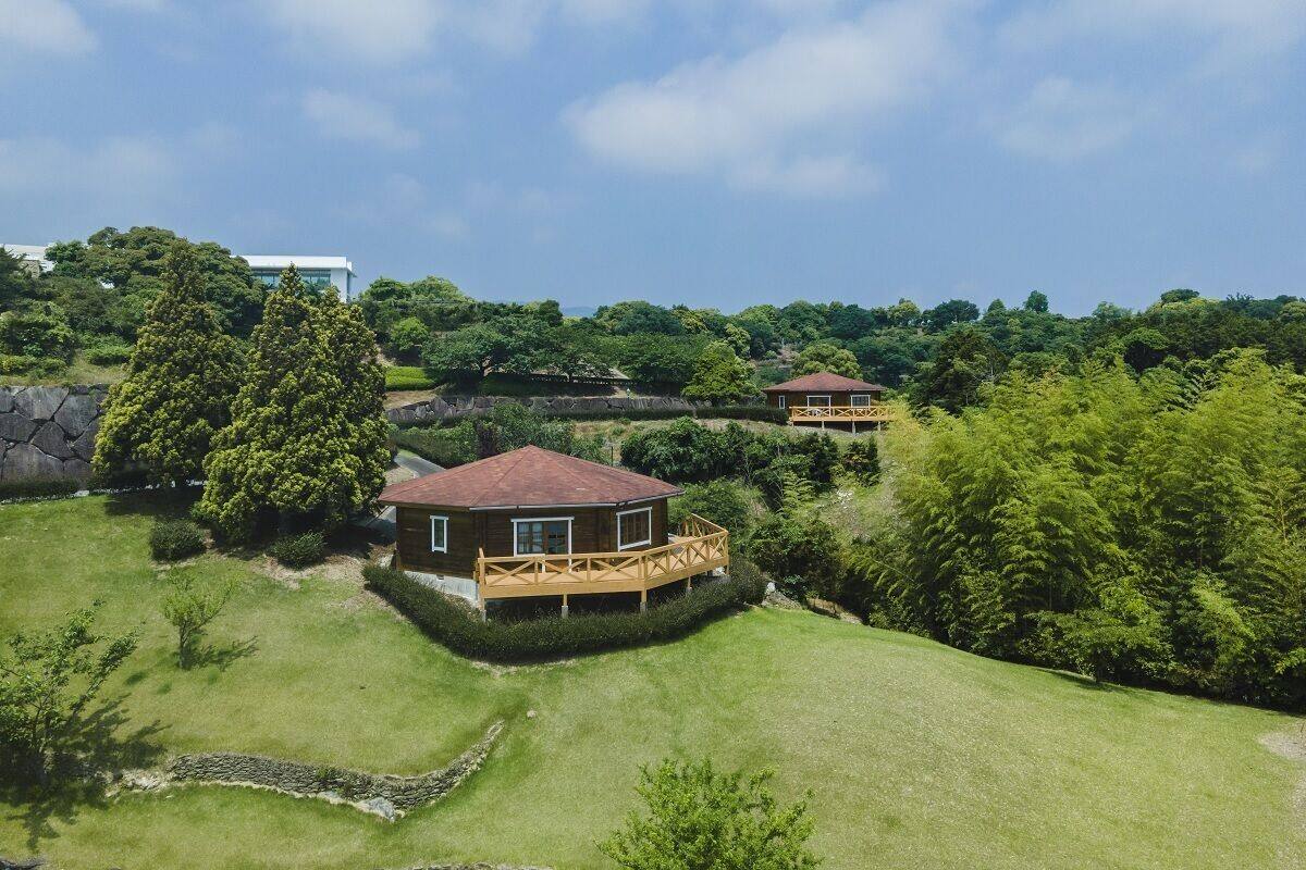 A house with a wooden deck and a red roof, surrounded by lush greenery and trees.