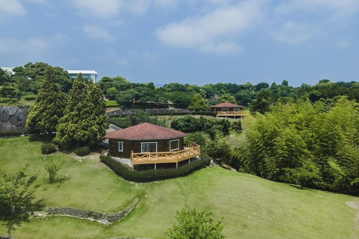 Una casa con terraza de madera y techo rojo, rodeada de exuberante follaje y árboles.