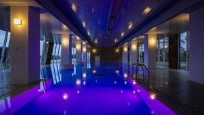 A modern indoor swimming pool with a glass enclosure, ambient lighting, and a stone accent wall. - Hotel Passage Kinkai (Nagasaki)