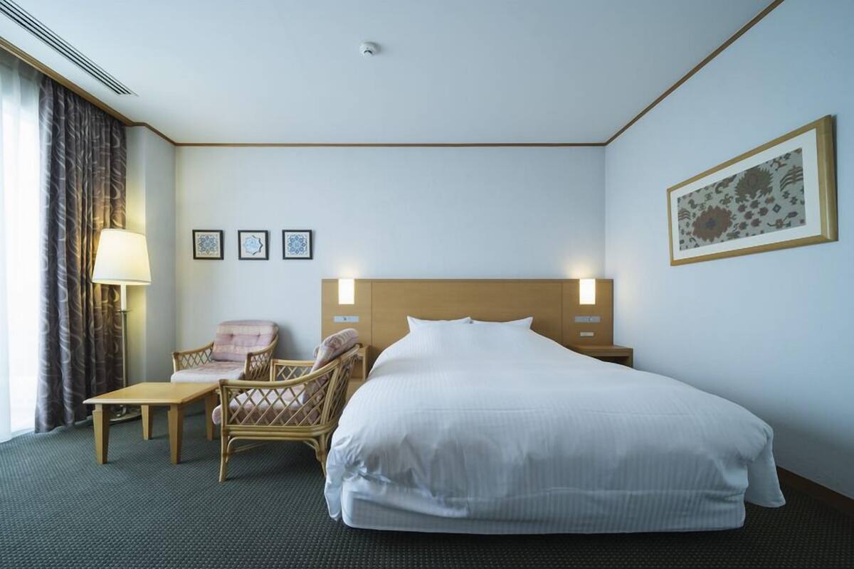 A hotel room with a large bed, two chairs, a small table, and a lamp.