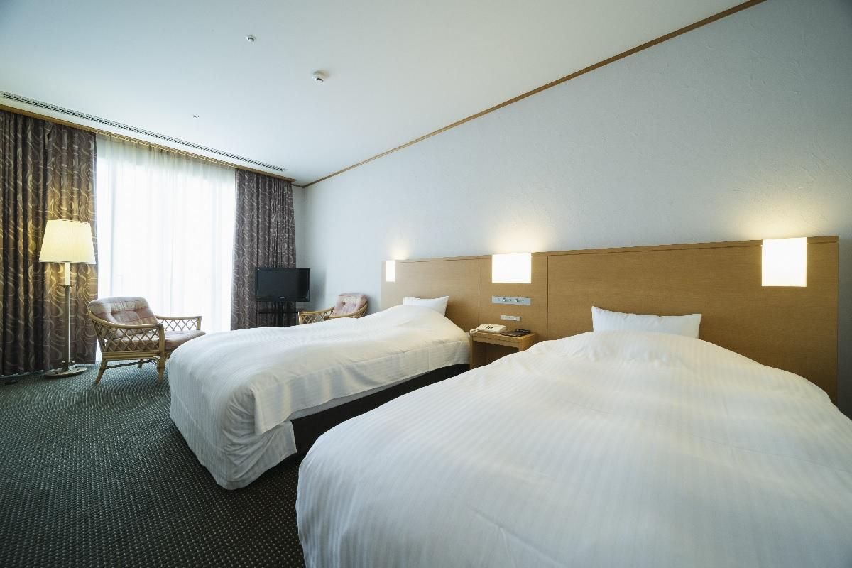 A hotel room with two beds, a chair, a desk, and a TV.