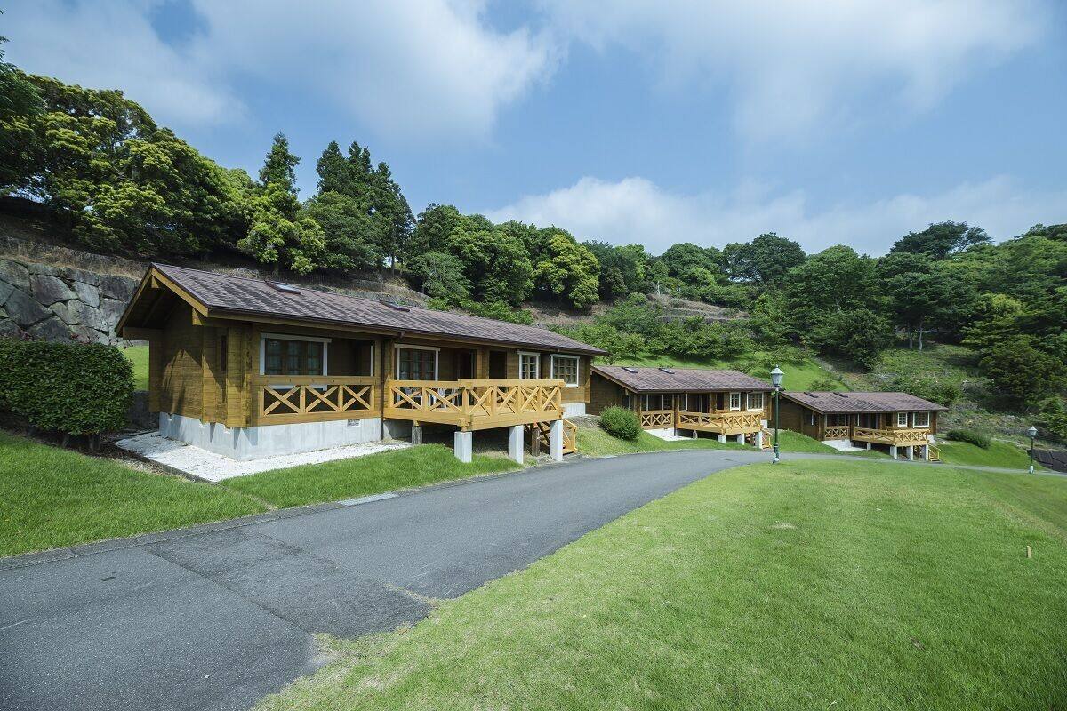 A row of wooden cabins with a stone wall and a paved path leading to them.