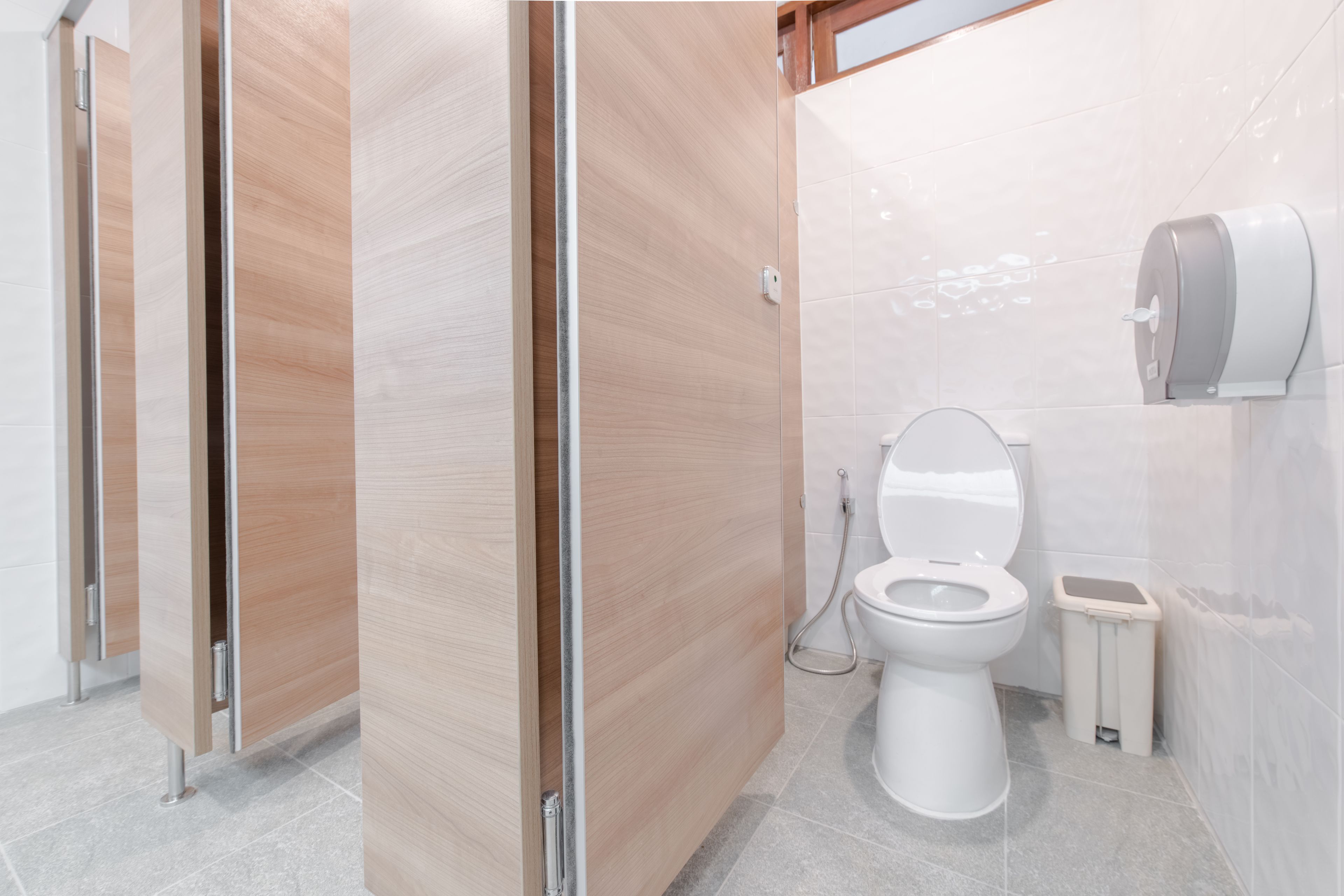 A modern bathroom with wooden partitions, a toilet, a bidet, and a trash bin.