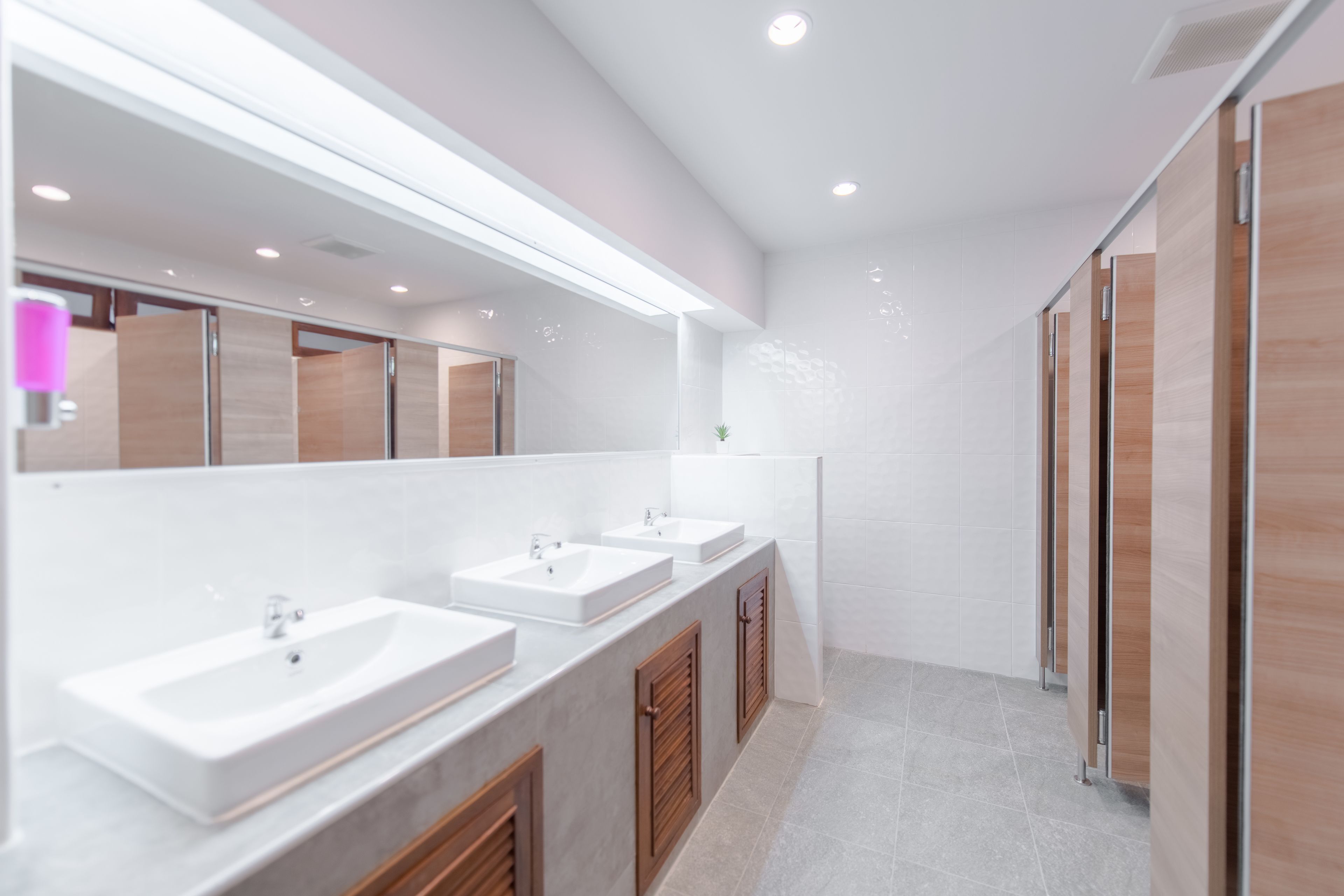 A modern bathroom with three sinks, wooden cabinets, and a large mirror.