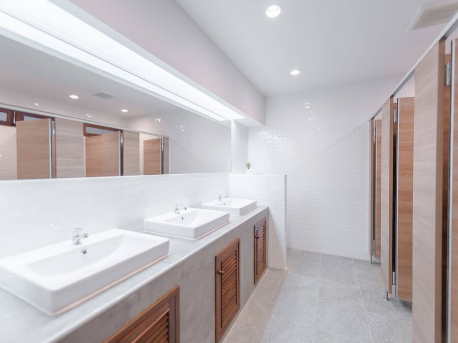 A modern bathroom with three sinks, wooden cabinets, and a large mirror.
