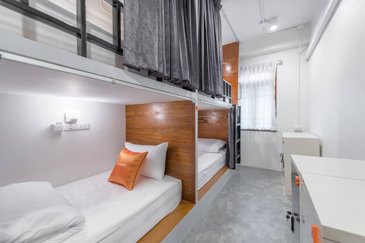 A compact hotel room with bunk beds, a small desk, and a window with curtains.
