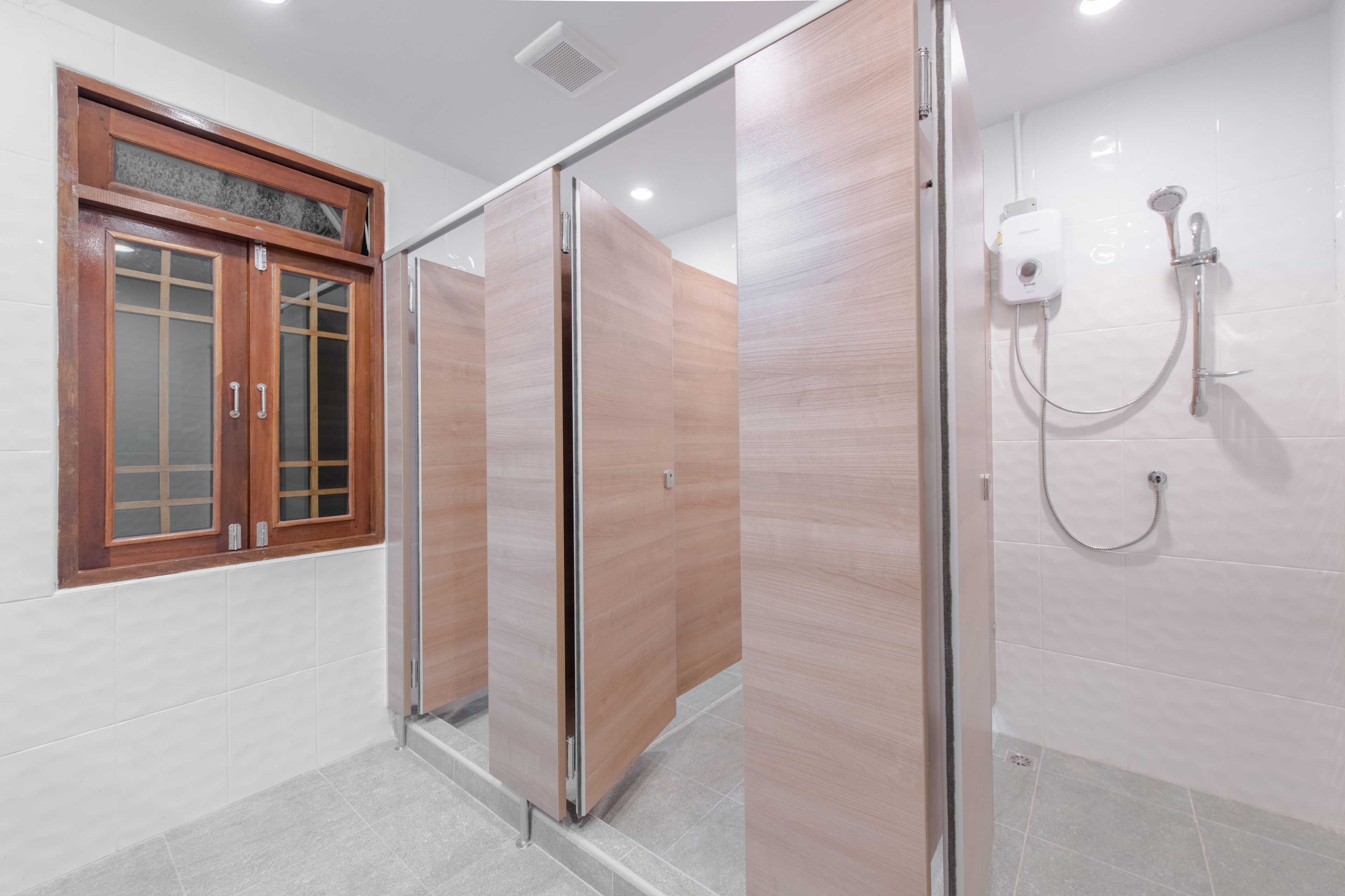 A modern bathroom with a wooden vanity, a shower with a handheld showerhead, and a window with frosted glass.