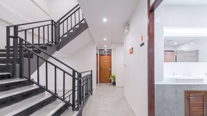 A modern interior with a staircase, a hallway leading to a door, and a bathroom with a sink and mirror. - Tiny Taladnoi Hostel (Bangkok)