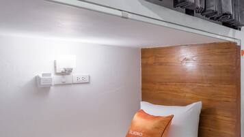 A bunk bed with a white mattress, an orange pillow, and a wooden headboard.