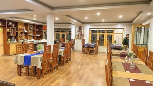 A restaurant with wooden tables and chairs, a counter, and a large window. - Hotel Grand Nubra (Leh)