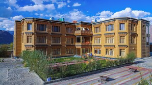 A multi-story hotel with balconies, a courtyard with seating, and a mountainous backdrop. - Hotel Grand Nubra (Leh)