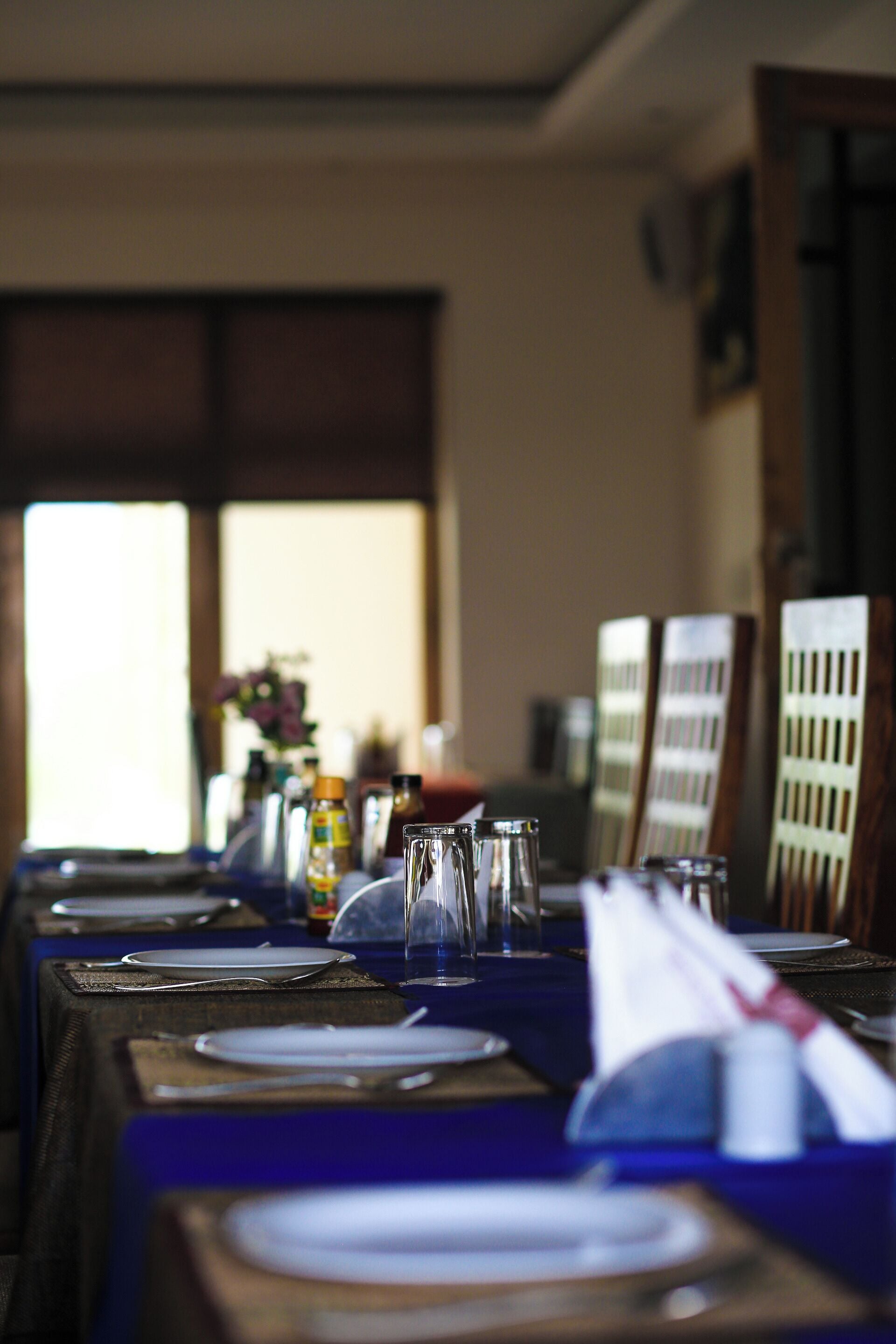 A dining table set with plates, cutlery, and glasses, with a window in the background.