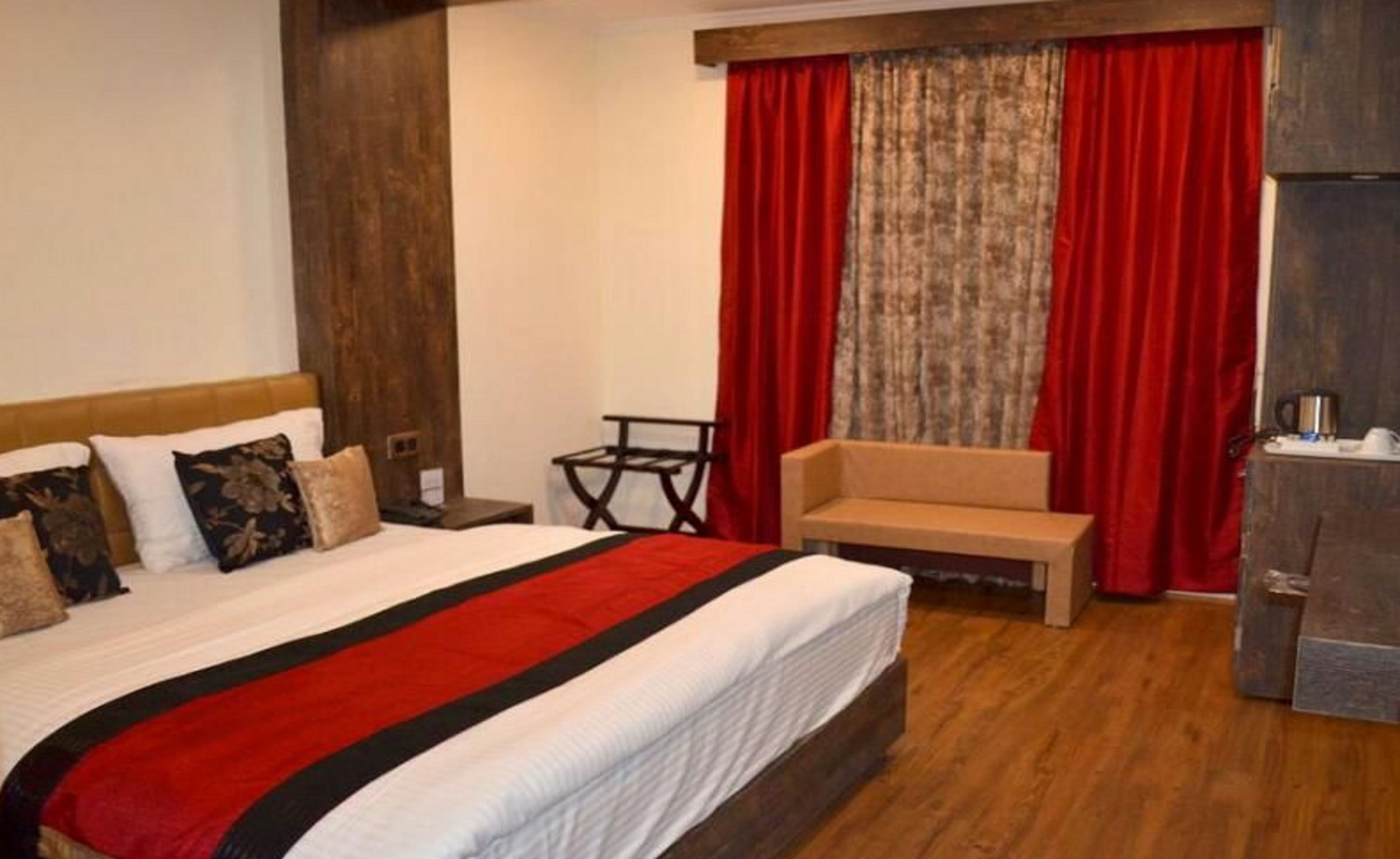 Quarto de hotel com uma cama grande, cabeceira de madeira, uma mesa pequena, um sofá e uma escrivaninha com chaleira.