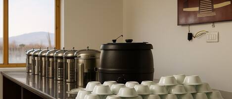 A kitchen counter with stainless steel containers, a large black pot, and white cups arranged on it.