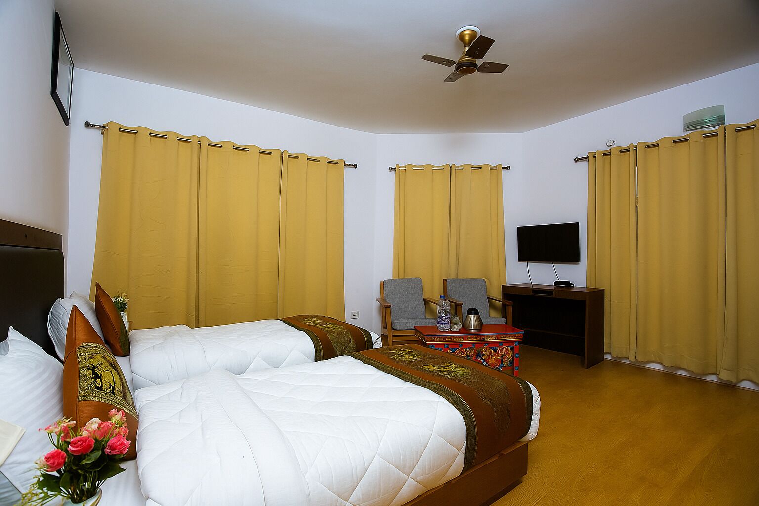 A hotel room with a bed, two chairs, a desk, a television, and a ceiling fan.