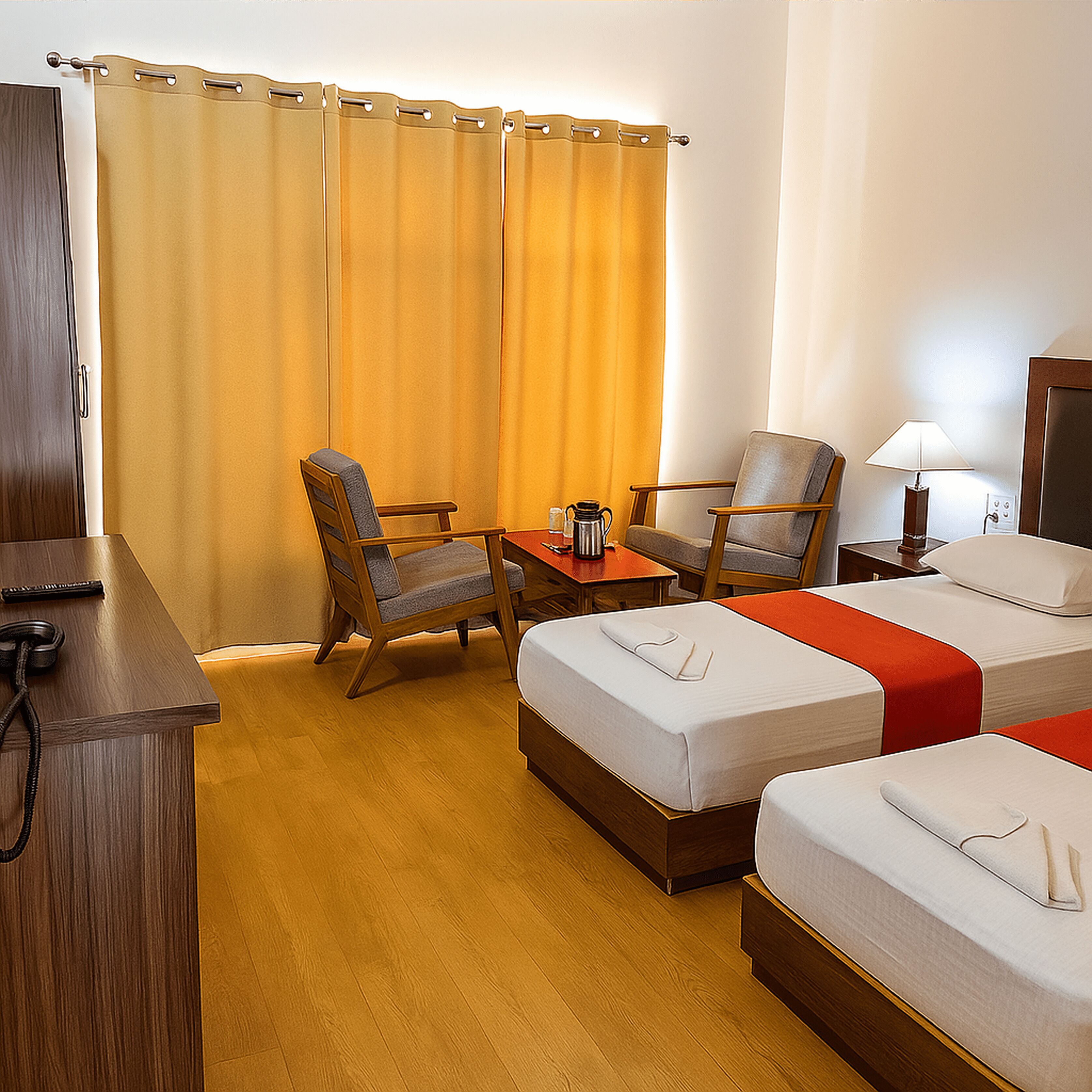 A hotel room with two single beds, a desk, two chairs, a table with a coffee pot, and a lamp.