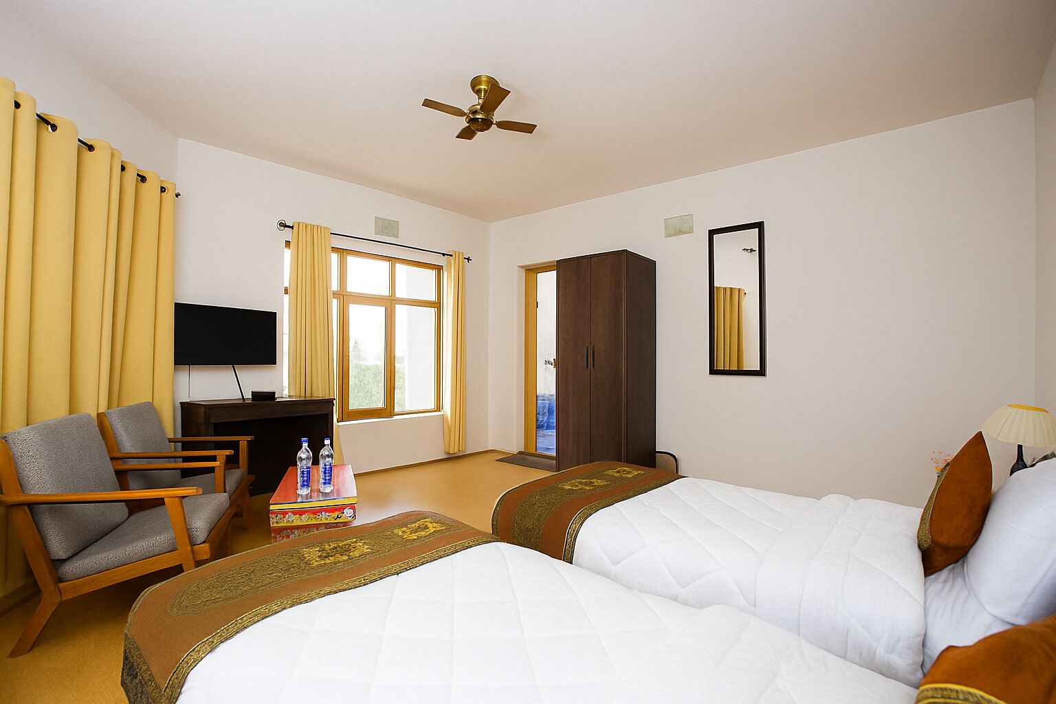 Habitación de hotel con dos camas, un escritorio, una silla, un televisor y un armario.