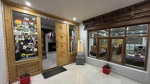 A hotel lobby with a wooden door adorned with stickers, a tiled floor, and two potted plants. - Hotel Grand Nubra (Leh)