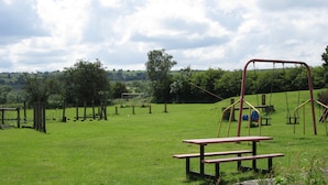 A picnic table in a grassy field with playground equipment in the background.