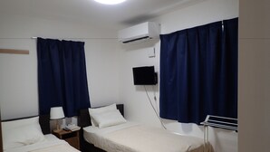 A hotel room with two single beds, a flat-screen TV mounted on the wall, and an air conditioning unit.